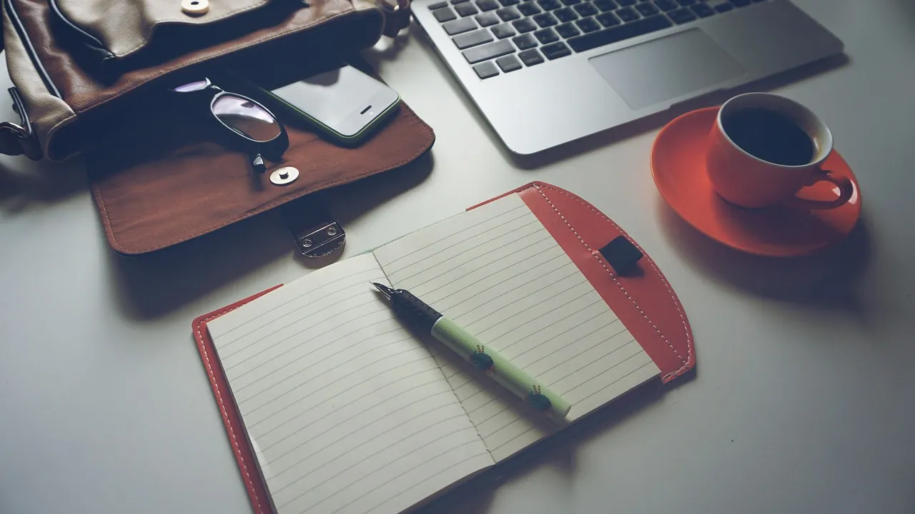Carnet ouvert et stylo posés sur un bureau, à côté d’une tasse